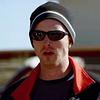 A photo of Breaking Bad character Jesse Pinkman wearing sunglasses, a beanie, and a red hoodie with a black shirt underneath